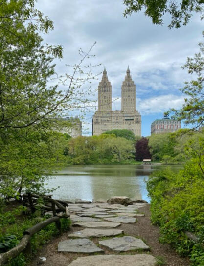 Photo by Shefali Parekh Stone path leading to the edge of a lake in Central Park. In the background is an iconic residential building.